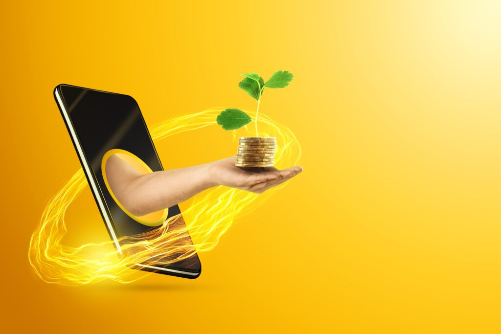 A hand holds money in the palm, coins with a green sprout through a smartphone on a yellow background. The concept of online lending, money at interest, savings growth, online bank