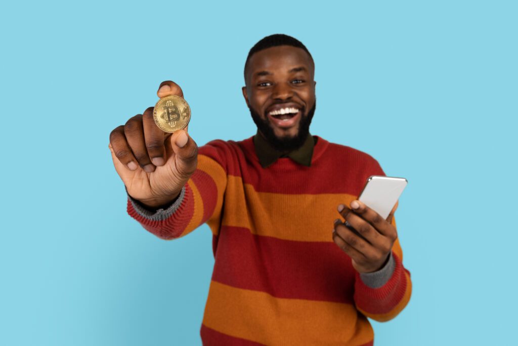 young man happily holding 1 bitcoin and a smartphone
